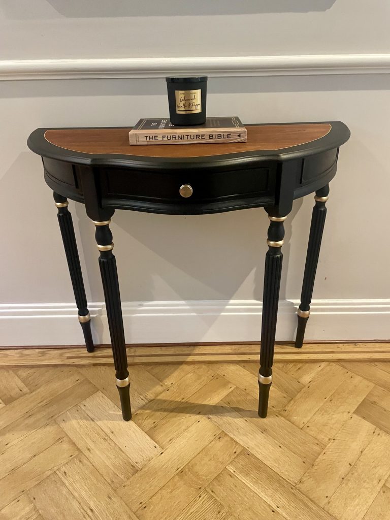 The Demi-Lune Console with a candle and books on its wood veneer top